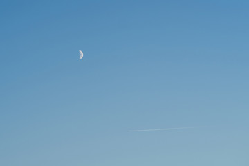 Airplane in blue sky faraway with moon on background