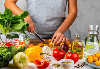 Woman cuts yellow cherry tomatoes and cooking salad in the kitchen. Healthy diet concept.
