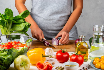 Woman cuts onions and makes salad in the kitchen. Healthy diet concept.