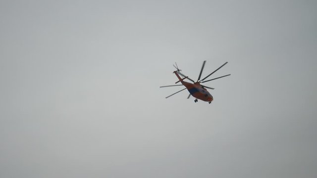 An orange helicopter in flight. A fire department helicopter flies against a grey sky.