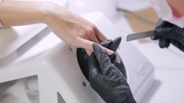 A manicurist in gloves nails the client with a nail file before applying the gel coating