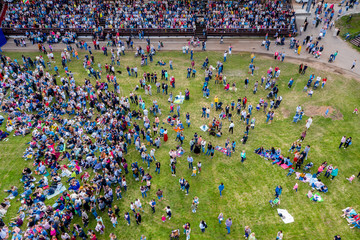 A large crowd of people are placed on the podium, standing and sitting on the grass in front of the...