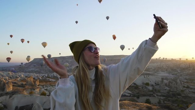 Young blond female traveler blogger taking selfie with air balloons slow motion