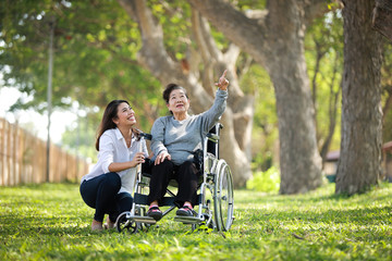 Plakat Asian senior woman sitting on the wheelchair with her daugther family happy smile face on the green park
