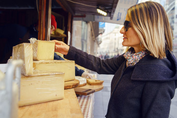 Portrait of caucasian woman female tasting and buying organic french cheese on the street market sail saint nectaire or brie in winter or autumn day in europe or america