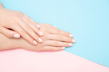 Beautiful female hands with stylish nail manicure gel polish on pink and blue background, top view....