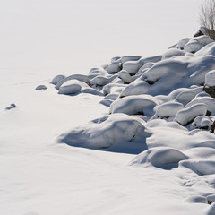 Eingeschneiter See mit Steinen am Uferrand