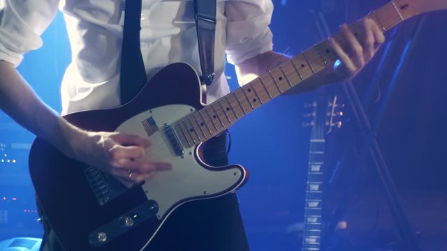 Guitarist in a white shirt and black tie plays rythm guitar and dances on stage