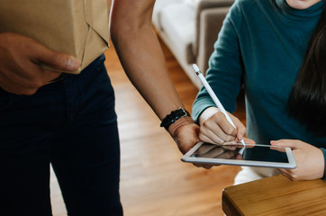 asian woman customer appending signature in digital mobile tablet receive parcel box from home...