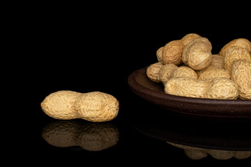Lot of whole tasty beige peanut closeup with brown ceramic coaster isolated on black glass