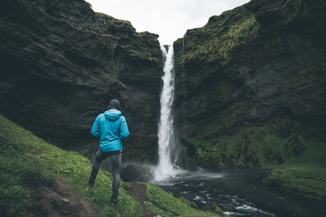 young man standing infront of the Kvernufoss waterfall near skogafoss in southern iceland watching the water flow enjoying his travel