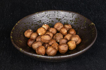 Lot of whole tasty brown hazelnut in glazed bowl on grey stone