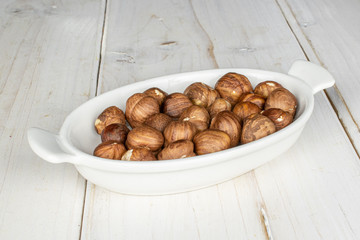 Lot of whole tasty brown hazelnut on white ceramic plate on white wood