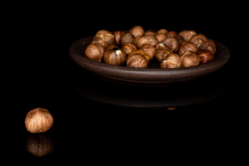 Lot of whole peeled tasty brown hazelnut with brown ceramic coaster isolated on black glass
