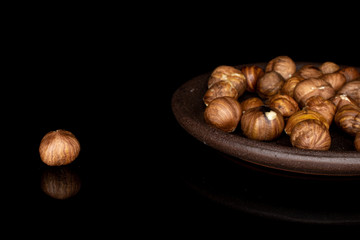 Lot of whole tasty brown hazelnut with brown ceramic coaster isolated on black glass