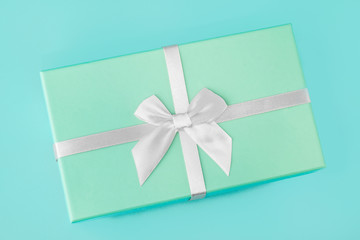 Gift box with a white silver bow, mint green on a mint turquoise background. Holiday gift minimal concept. Top view, flat lay, close-up.
