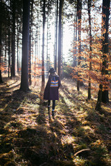 Fototapeta premium Young woman with backpack is walking through the forest at beautiful autumn sunset.