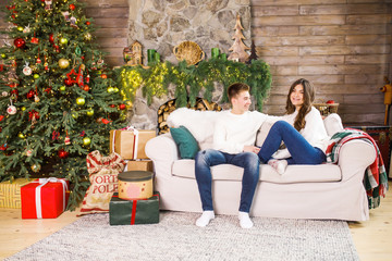 Obraz premium young beautiful couple sitting in a beautiful room on the bed against the background of the Christmas tree and smiling