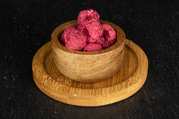 Lot of whole dried raspberry on round bamboo coaster in bamboo bowl on grey stone