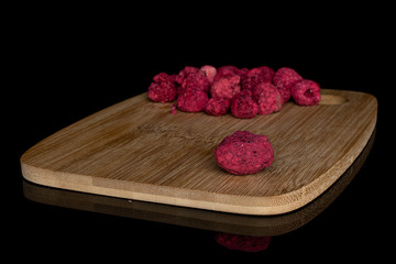 Lot of whole dried raspberry on bamboo cutting board isolated on black glass