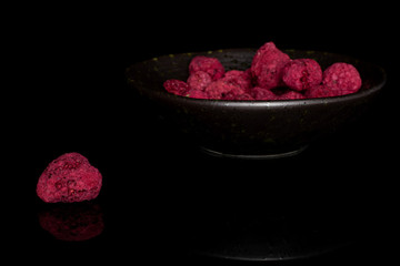 Lot of whole dried raspberry in glazed bowl isolated on black glass