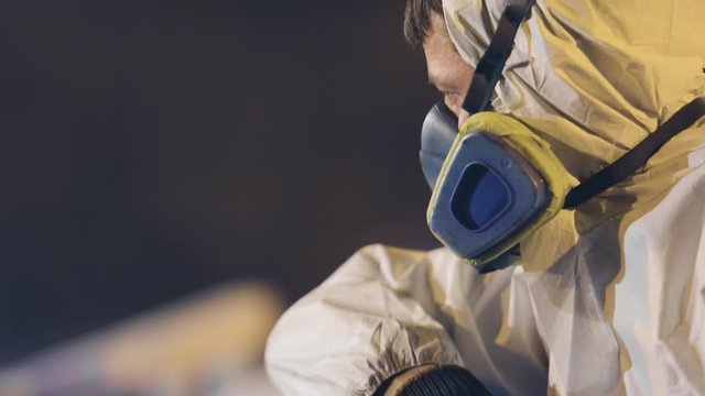 A man in a protective suit paints a large part, a spray gun, painting a large metal part