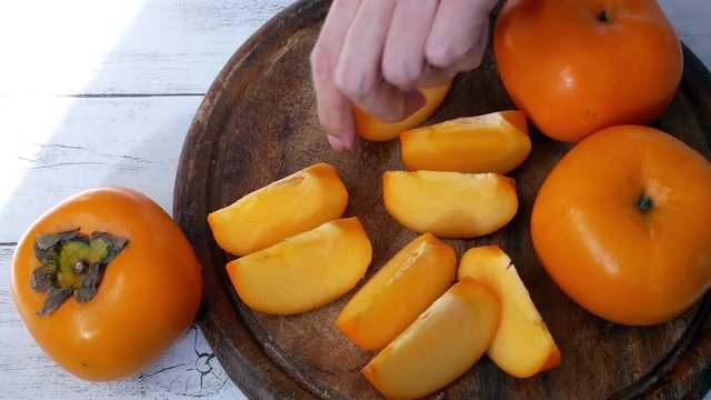 Woman hand take a sliced persimmon fruit from chopping board, natural light.