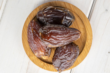 Group of four whole dried brown date fruit on round bamboo coaster flatlay on white wood