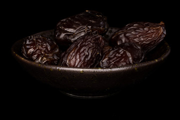 Lot of whole dried brown date fruit in glazed bowl isolated on black glass
