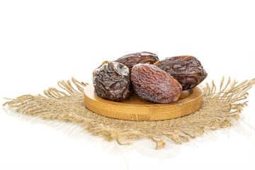 Group of four whole dried brown date fruit with jute fabric on round bamboo coaster isolated on white background