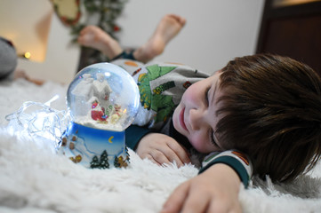 Boy looking a glass snow ball under a Christmas tree. Child with a snow ball with a New Year