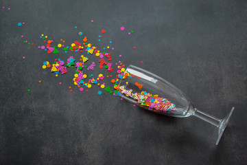 A wine glass from which multicolored splashes of colorful confetti in form of circles and birthday caps on a dark background. Copy space.The concept of a party, celebration, new year, Christmas