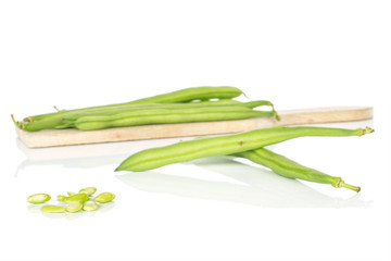 Lot of whole lot of pieces of snap green bean on wooden cutting board isolated on white background