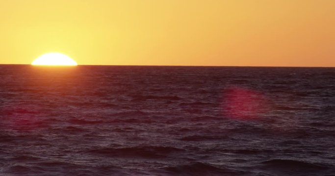 Slow Motion close up of sun ball setting behind ocean. Filmed at Zuma Beach in Malibu California.