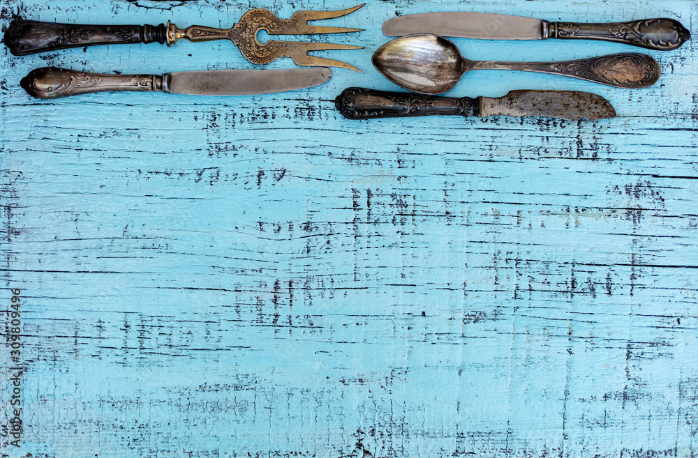 Wall mural Vintage cutlery - spoons, forks and knives on an old wooden background.