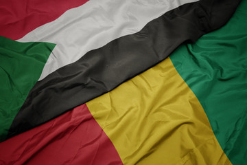 waving colorful flag of guinea and national flag of sudan.
