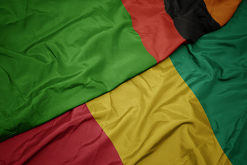 waving colorful flag of guinea and national flag of zambia.