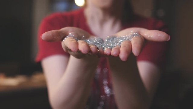 Woman blows off hands with silver sequins at the camera.