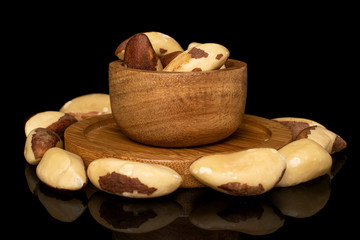 Lot of whole brazil brown nut in bamboo bowl on round bamboo coaster isolated on black glass