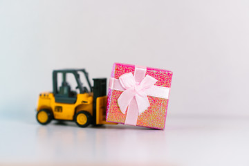Miniature forklift truck lift up pink gift box on white background