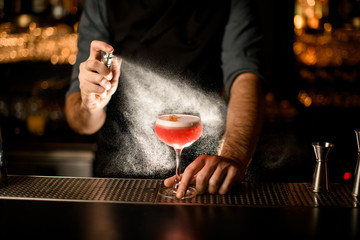 Bartender sprays small glass with alcohol drink