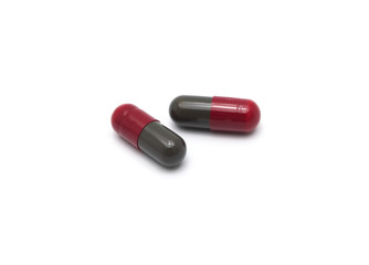 Prescription drugs, capsules of red and dark gray colors all mixed in. On white background.