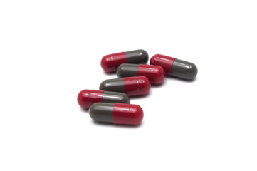 Prescription drugs, capsules of red and dark gray colors all mixed in. On white background.