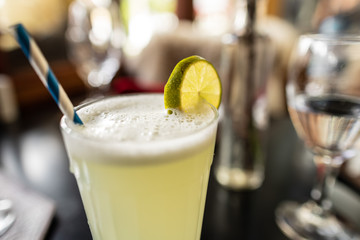 Copo de limonada sobre mesa escura com ambiente de restaurante desfocado ao fundo. 