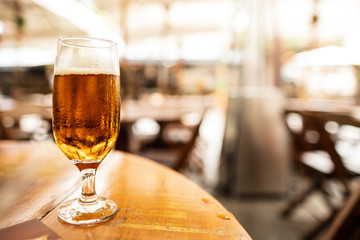 Taça de cerveja artesanal sobre mesa de madeira com ambiente de cervejaria desfocado ao fundo,.