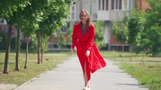 Happy young woman in the street. Beautiful young lady in passionate red dress is running happily on the city building background. Slow motion.