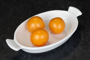 Group of three whole fresh orange physalis on white ceramic plate on grey stone