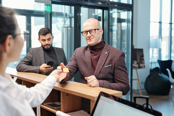 Business traveler in formalwear passing plastic card to hotel receptionist