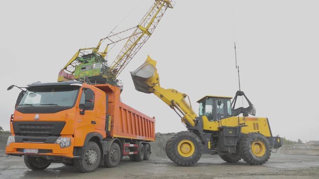 Loading a truck in the port, port crane work, port workflow. The excavator loads into the material in the truck