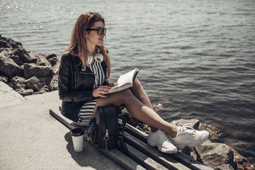 Outdoor Summer Portrait of Young Beautiful Girl in Black Leather Jacket and Glasses Reads the Book...